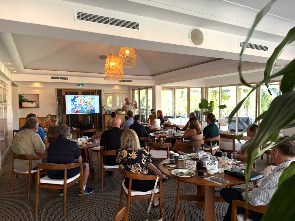 Mathew Hoffman standing at the front of the room, presenting to Noosa Business Group members seated at breakfast tables.